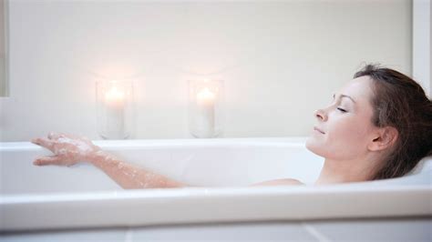 Tehotná žena relaxuje vo vani s teplou vodou, sviečky v pozadí.