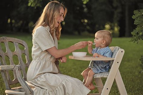 Dieťa sediace v jedálenskej stoličke, ktoré s nadšením sleduje rodiča pri jedle.